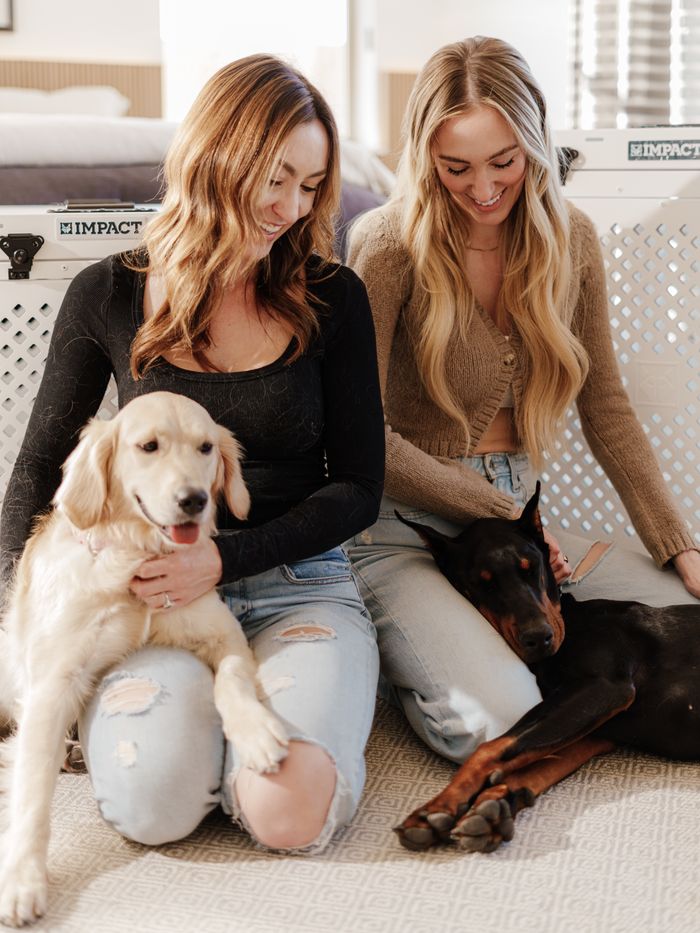 Two women with a Golden Retriever and a Doberman relaxing indoors.